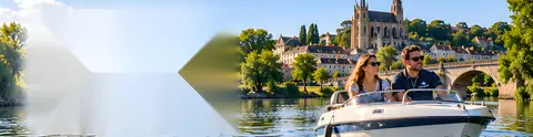 Un couple navigue sur une rivière à bord d'un bateau à moteur, devant un village et une cathédrale